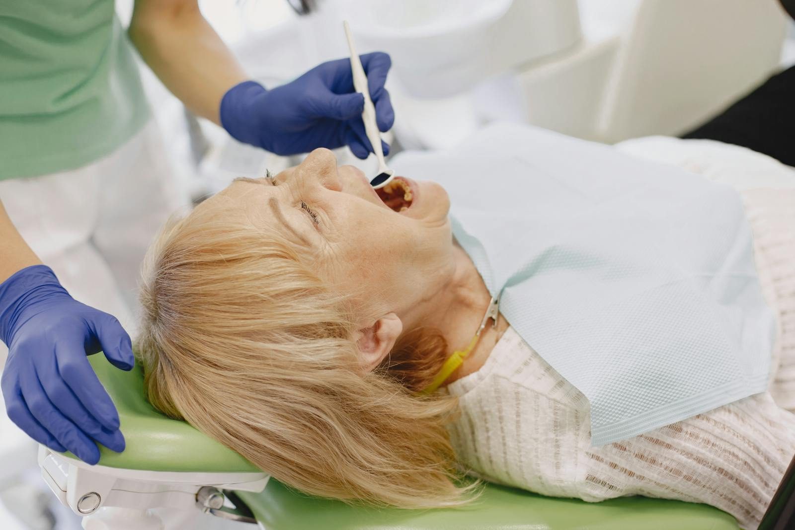 Elderly woman getting a dental examination from a dentist wearing gloves in a clinic.