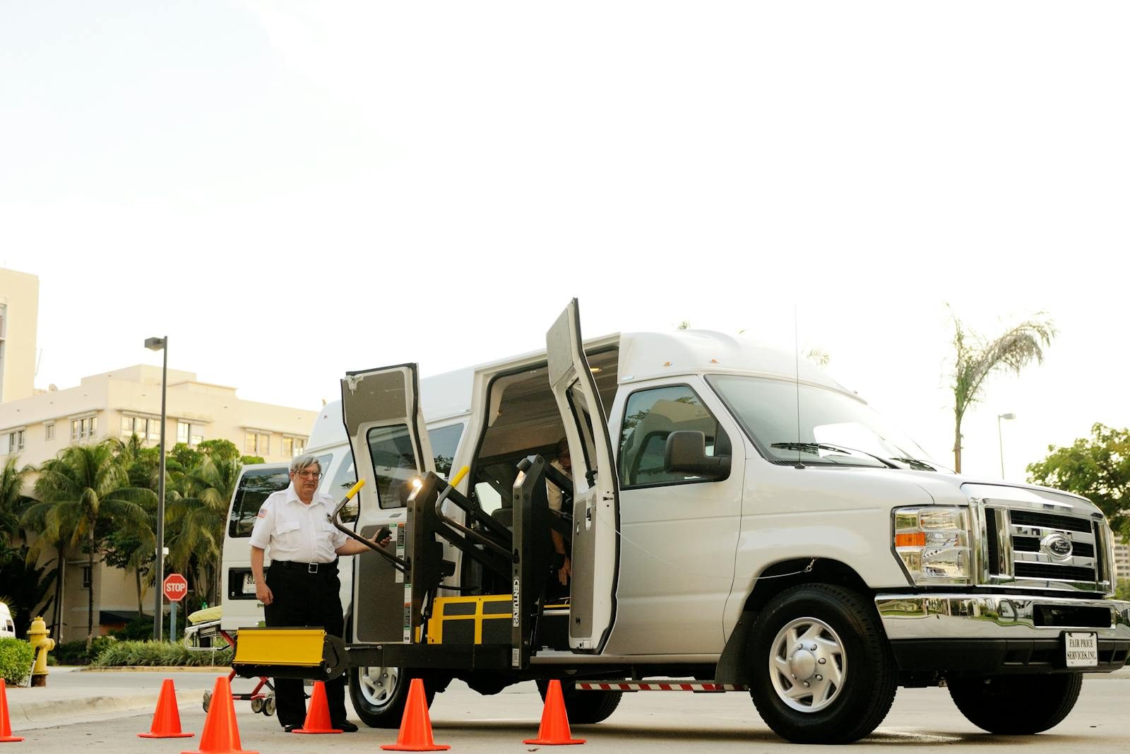 A driver standing by a wheelchair accessible van with open doors and a ramp, surrounded by cones.