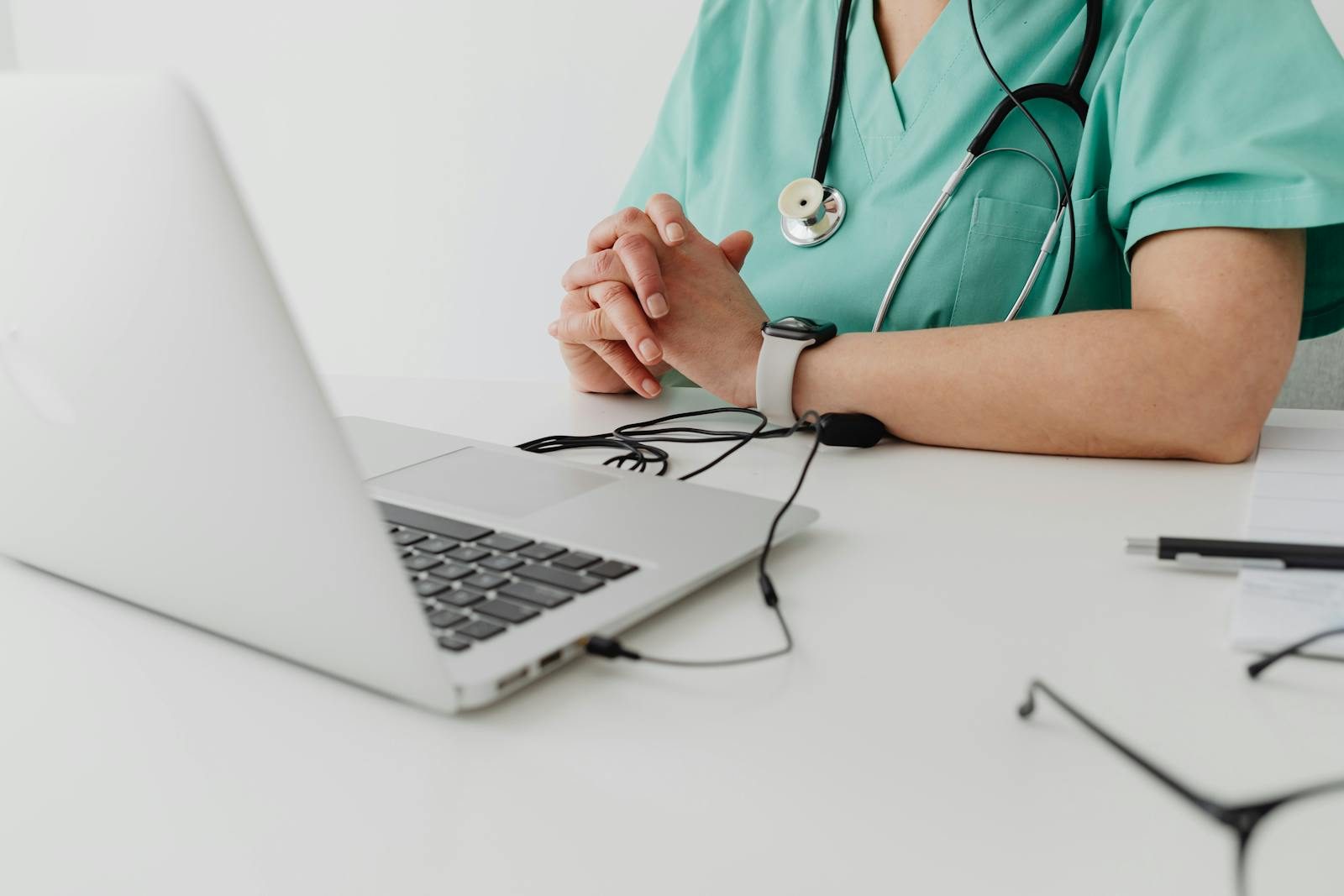 Medical practitioner in scrub suit using a laptop for remote consultation and documentation.