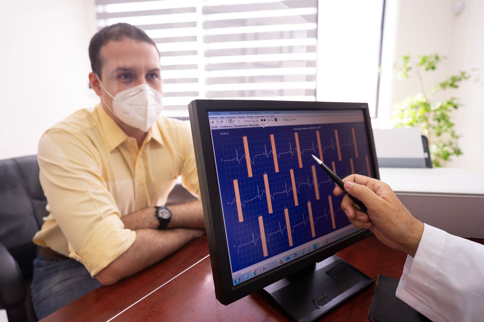 Medical consultation as a doctor reviews ECG results with a masked patient in a clinic setting.