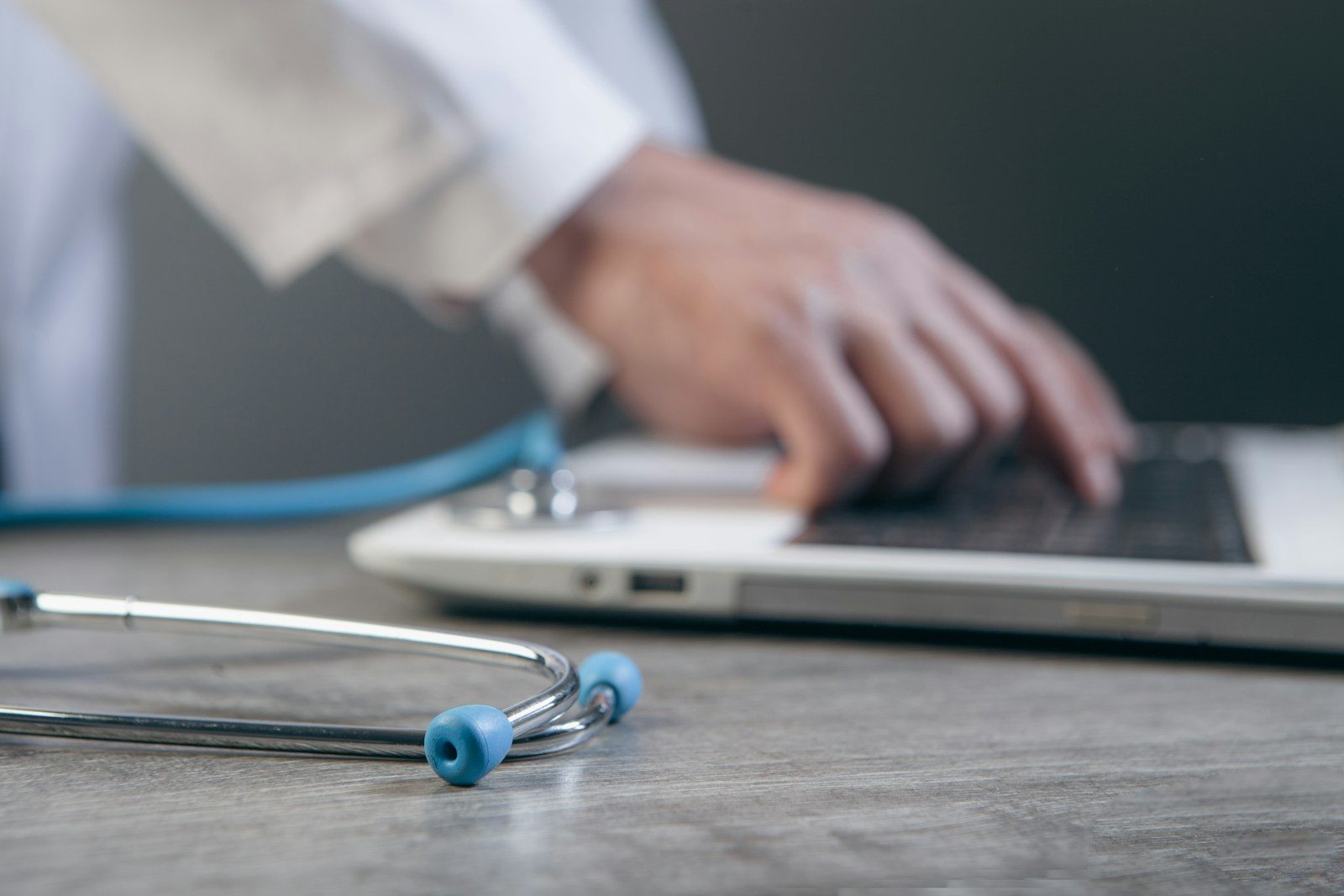 Doctor typing on a laptop with a stethoscope nearby.