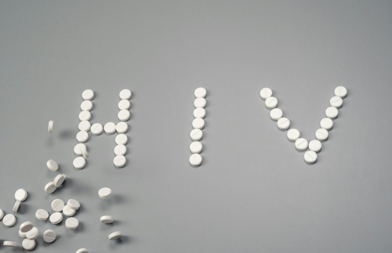 White pills forming the word 'HIV' on a grey background, symbolizing treatment.