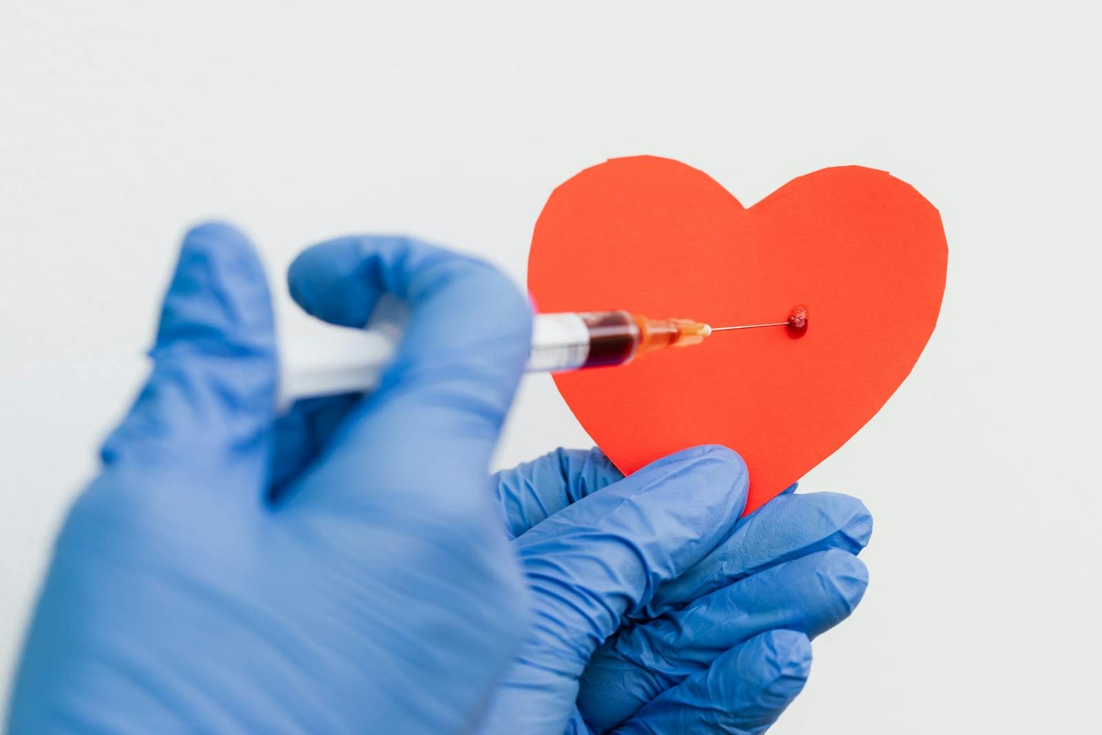 A conceptual image of a syringe injecting a red paper heart held by gloved hands, symbolizing health or love.